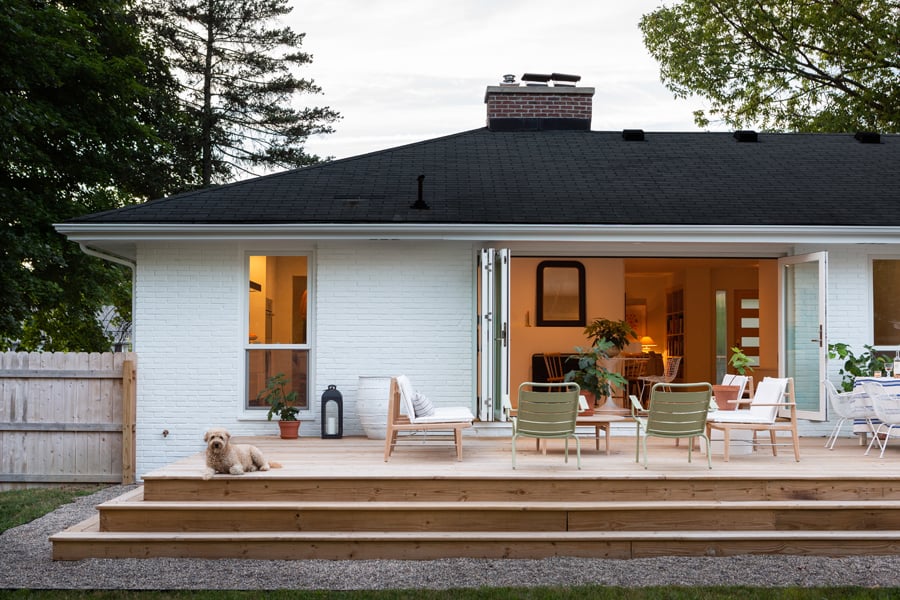 A white-painted Ranch home with an Andersen Folding Outswing Door opening to the deck outside.