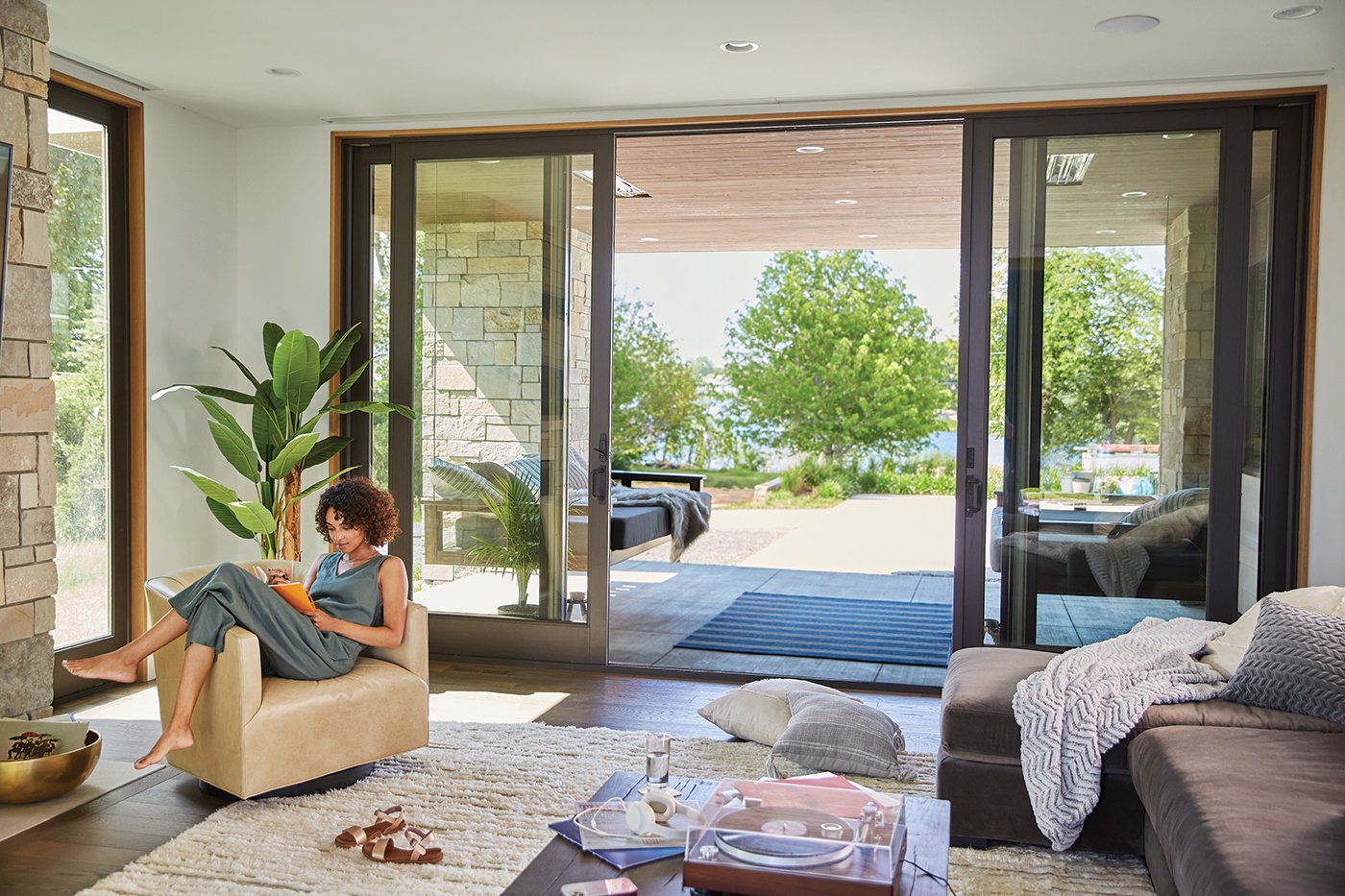 A woman lounges next to an open sliding glass door with a lake view.