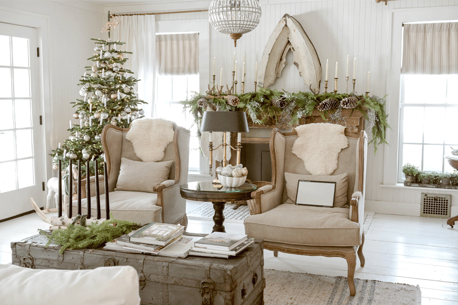A living room decorated with a Christmas tree, cozy fur throws, and a mantle covered in greenery, pinecones, and candles.