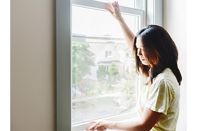 woman checking white framed Andersen window for hurricane season preparation