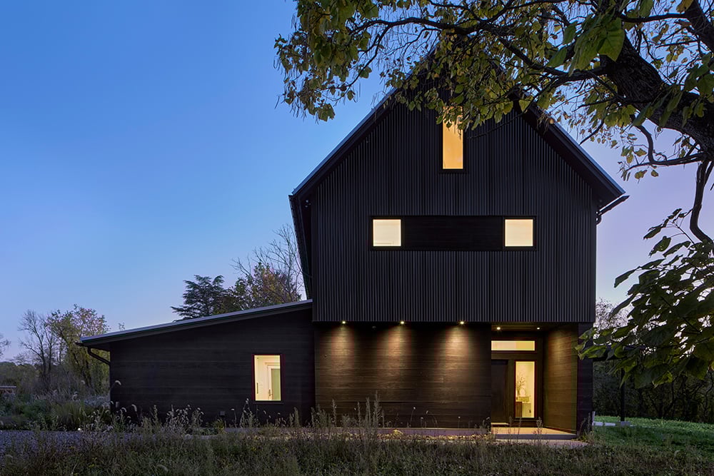 A black farmhouse with dark siding at dusk.   