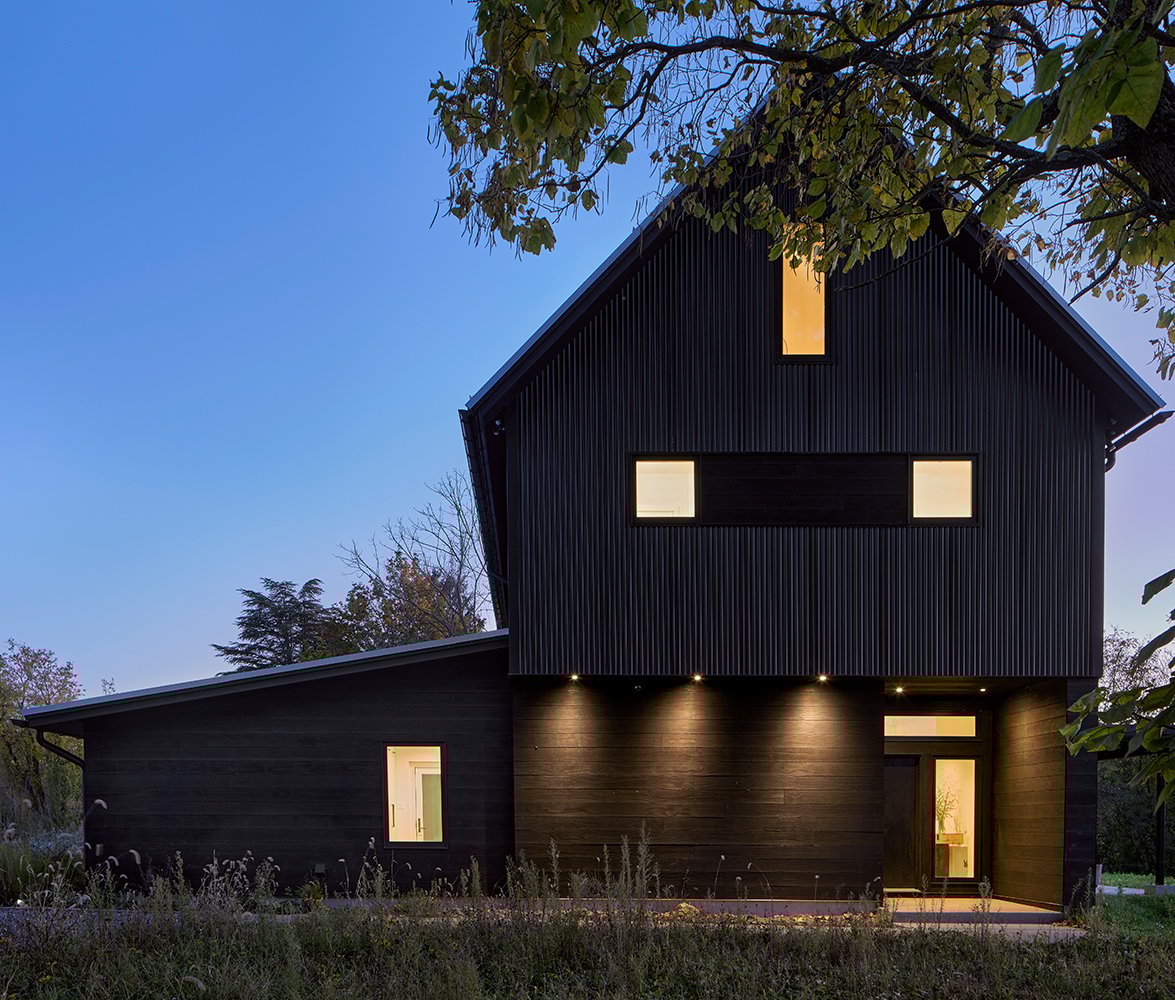 A black farmhouse with dark siding at dusk.