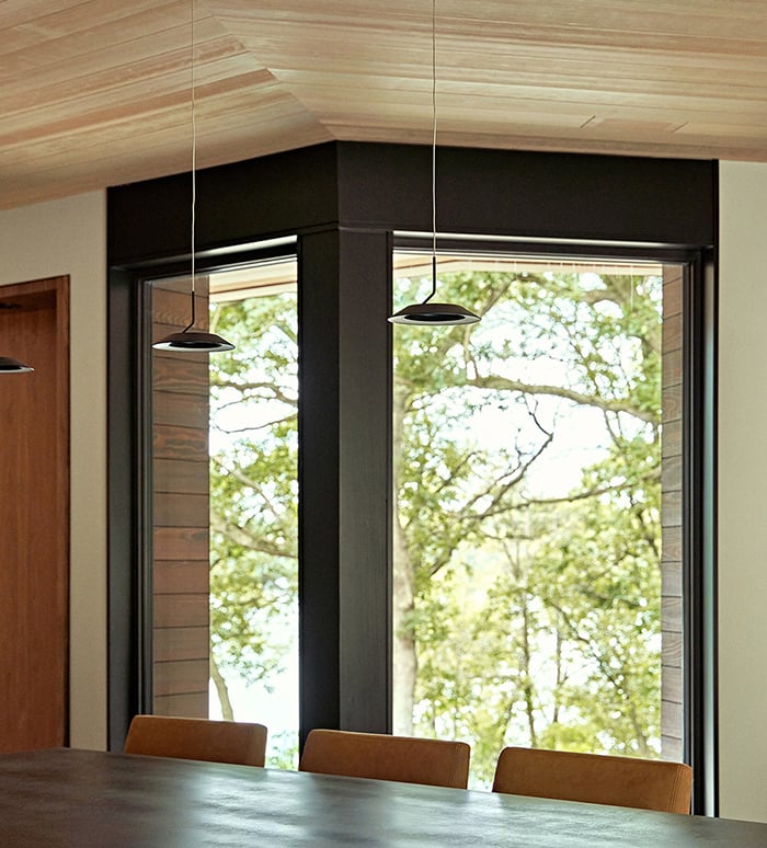 A kitchen where two floor-to-ceiling Andersen E-Series Picture Windows on either side of a bend provide views of a lake