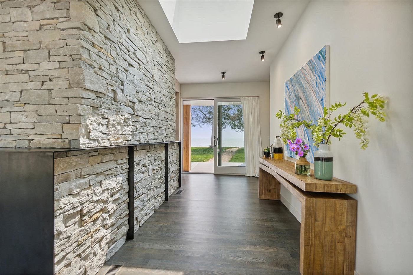 A hallway with grey stone on one wall leading to a gliding patio door with a view of a lake.  