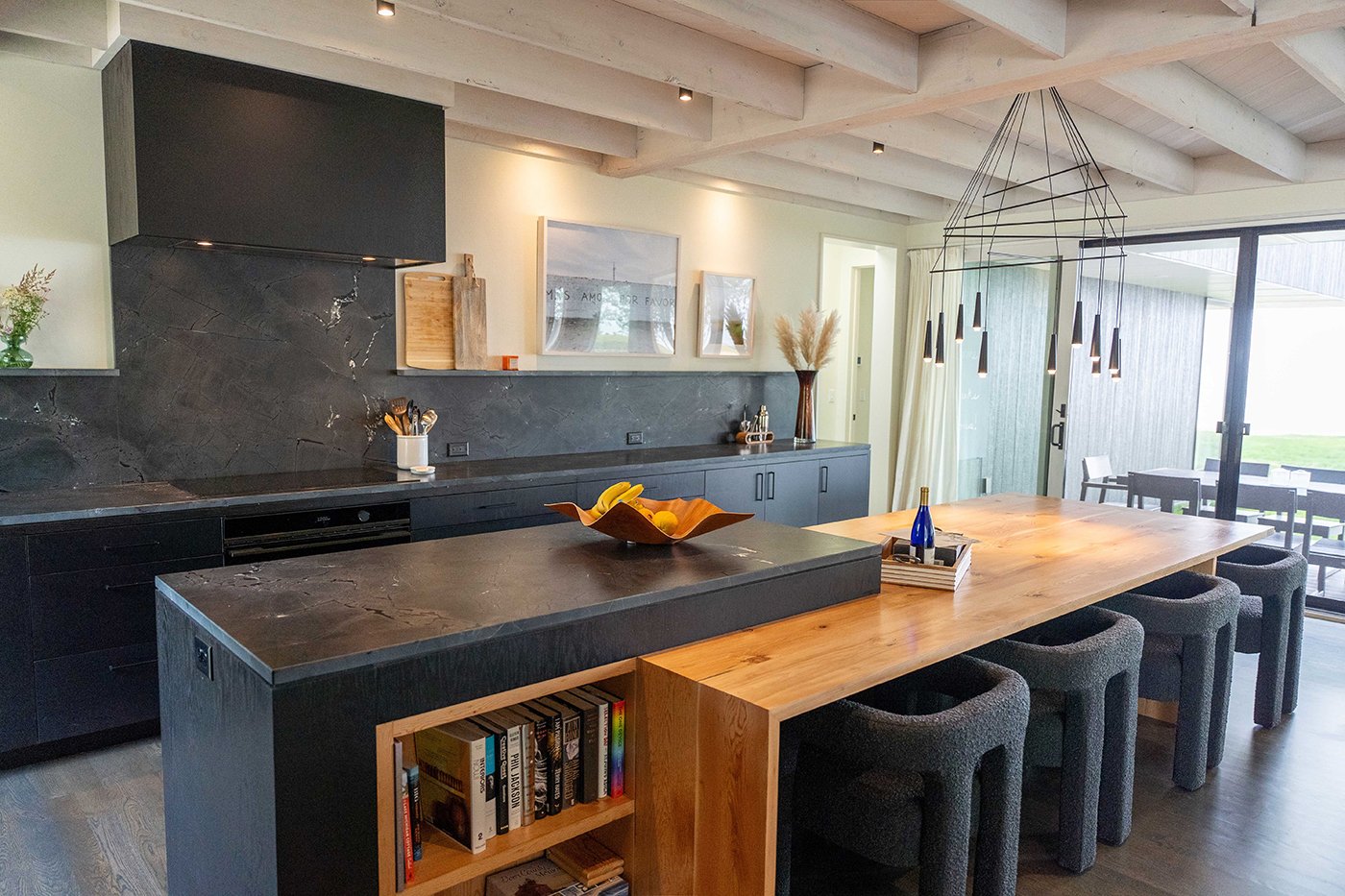 A kitchen with dark countertops and a wooden bar with gliding patio doors.