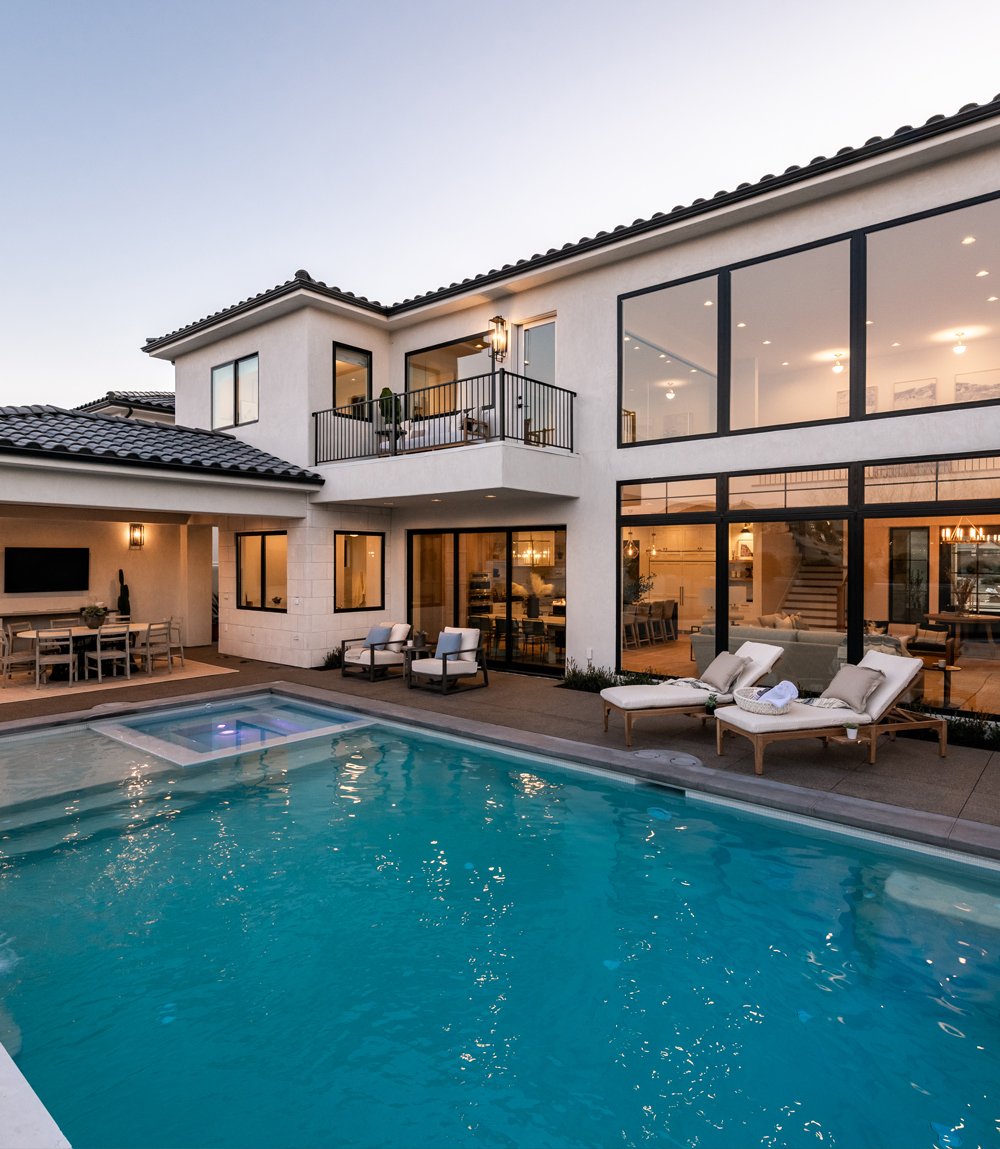 An outdoor dining area next to an underground pool with large, black windows and doors allowing deck access