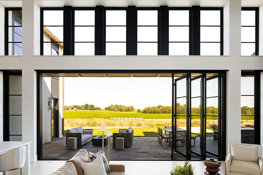A living room with a wall of glass created by an Andersen® Folding Outswing Door with a bank of picture windows above.