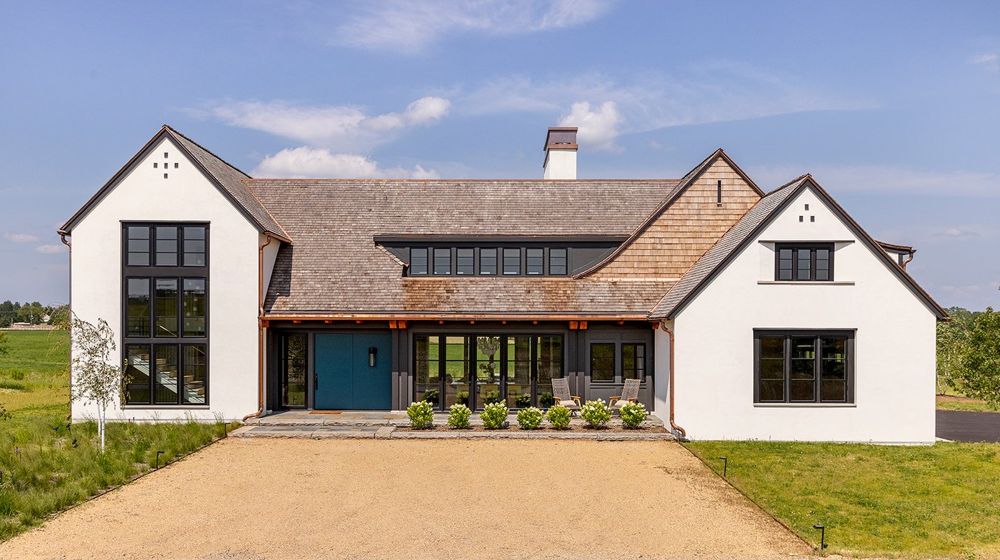 An exterior shot of a modern Tudor home with white stucco, black accents, and cedar shake roof.