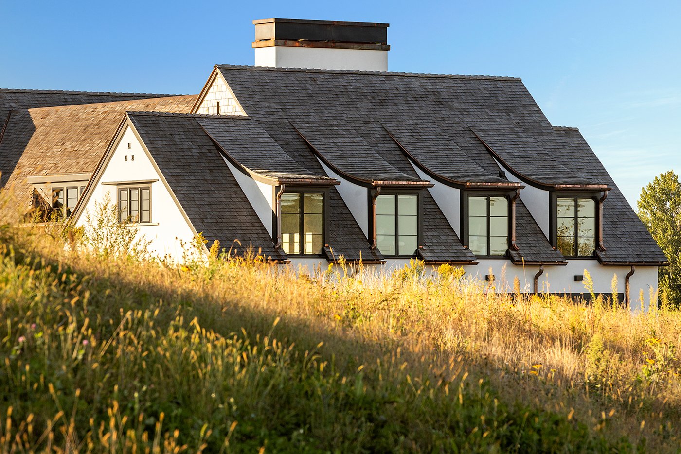A home with a row of four dormer windows peeks over a sunlit hill.