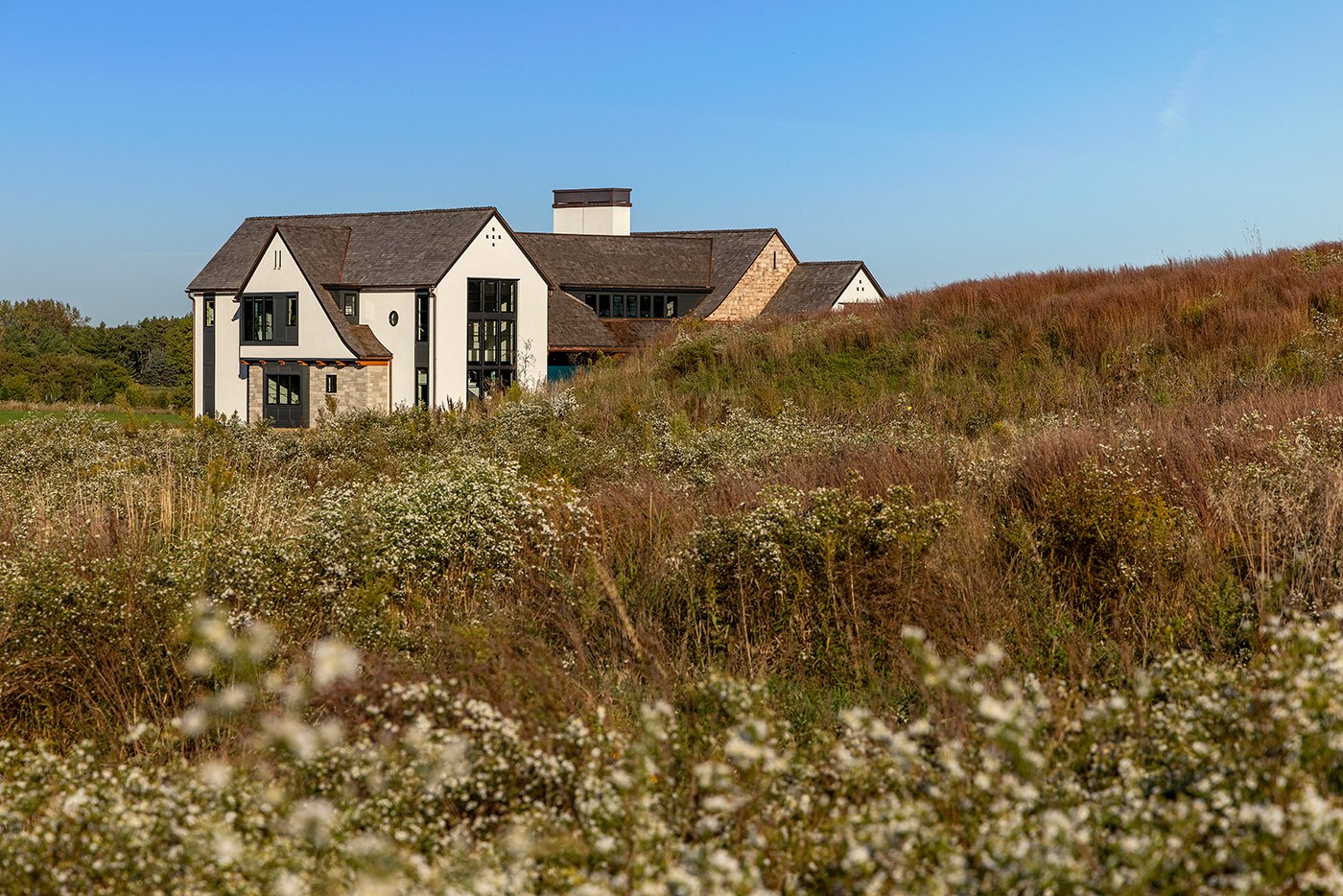 A prairie in bloom with a modern Tudor home rising up behind a hill.