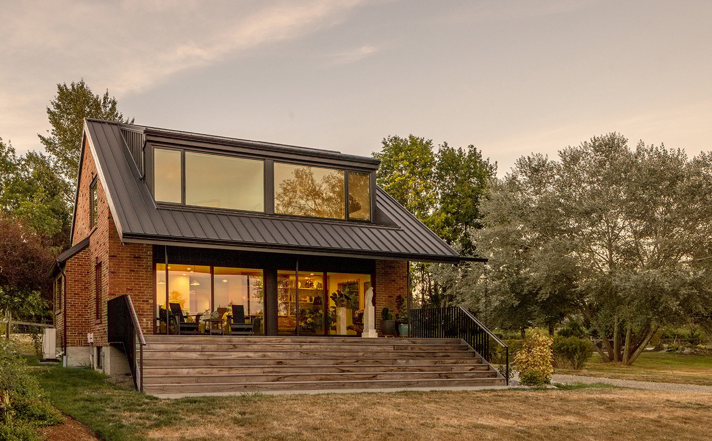 An exterior shot of a brick cottage with a black gable roof, brick siding and large windows with black frames.