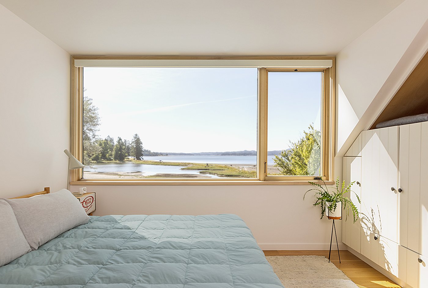 A bedroom with a picture and casement window with a view of the waterfront.