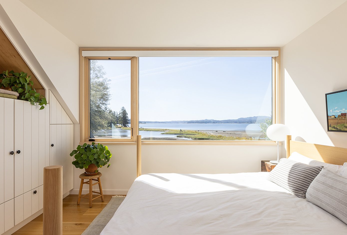 A bedroom with bright white walls and large windows with a view of the coast.