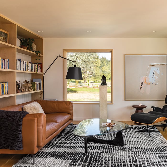 A room with a couch, recliner, bookshelves, artwork, and a square picture window.