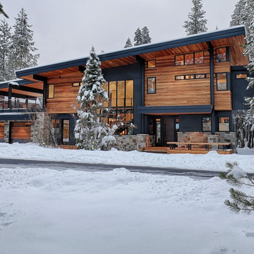Modern home with mixed materials and unique window shapes in a winter setting