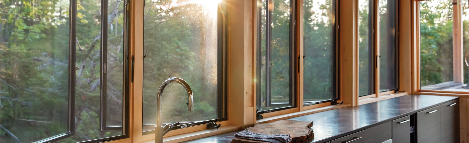 A kitchen that’s flooded with golden morning light through a row of Andersen® 400 Series Casement Windows with contemporary profiles.