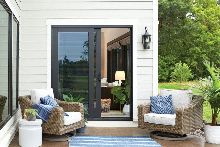 A black sliding patio door is featured with an outdoor patio that has two chairs.