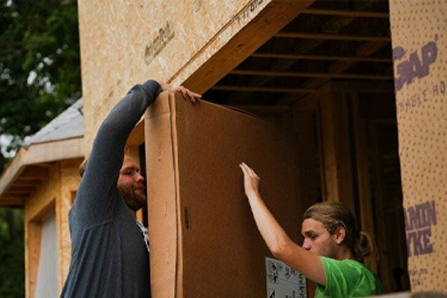 Two men carry a boxed-up window into a home that’s under construction.