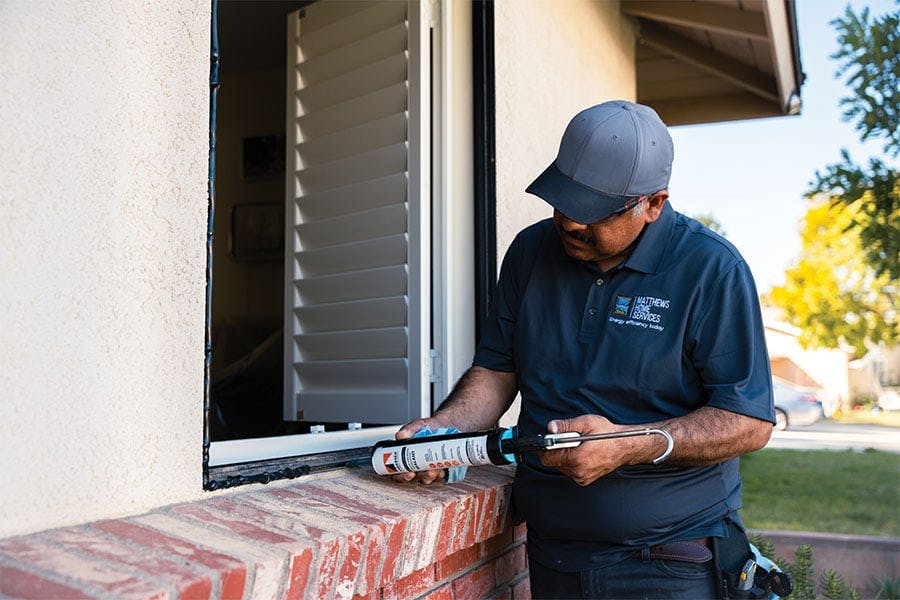 A person uses Andersen caulk to seal a window prior to installation. 