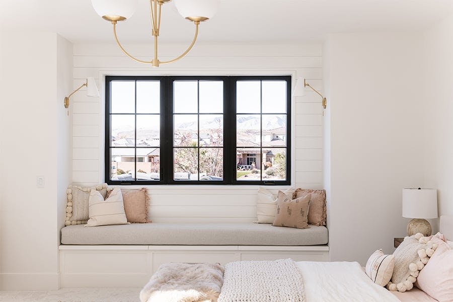  A bedroom with a neutral color scheme, shiplap walls, and three black-framed windows with a window seat underneath. 