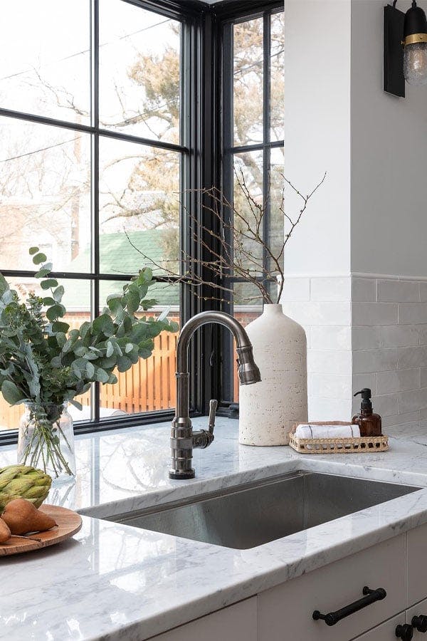 A garden window with black frames and colonial grilles in a kitchen with marble countertops and subway tile.