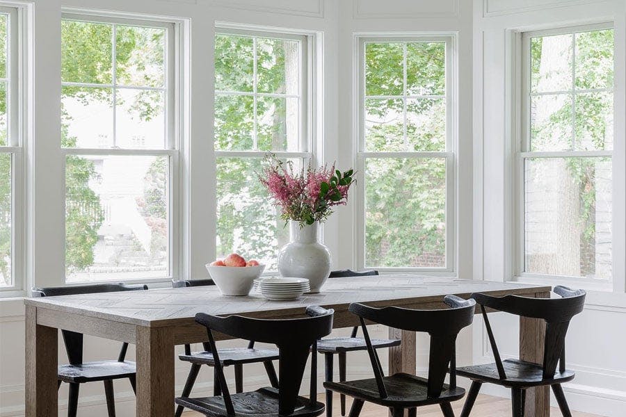 A breakfast room with a table is surrounded by several walls of white windows.
