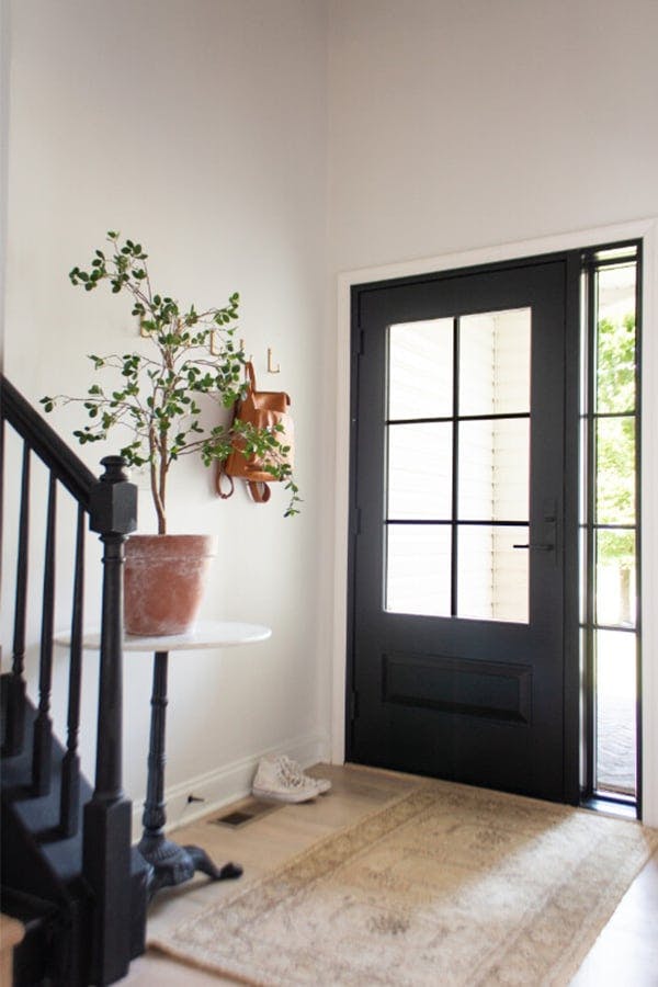 An entryway with a black staircase and wood floor, and a black front door with a large glass window with colonial grilles and matching sidelight.