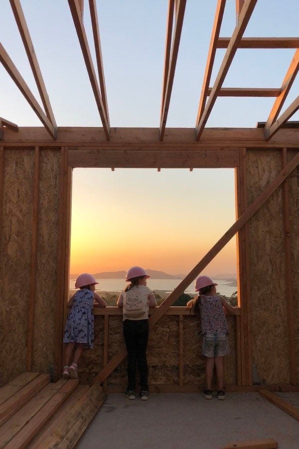 three people on construction site looking through opening of framed window at sunset