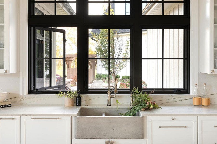 A European farmhouse kitchen featuring black casement windows over a rustic concrete apron sink 