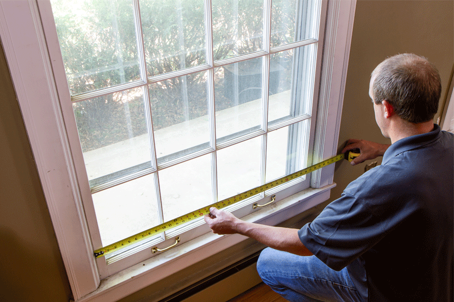 A man measures the width of a window from jamb to jamb. 