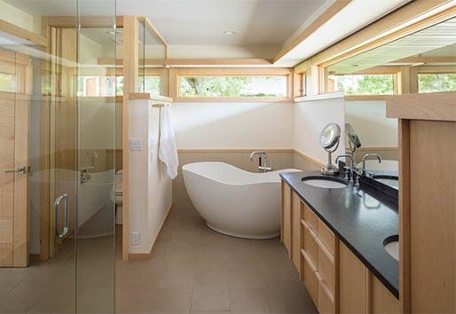white and wood bathroom with light wood windows over white freestanding tub