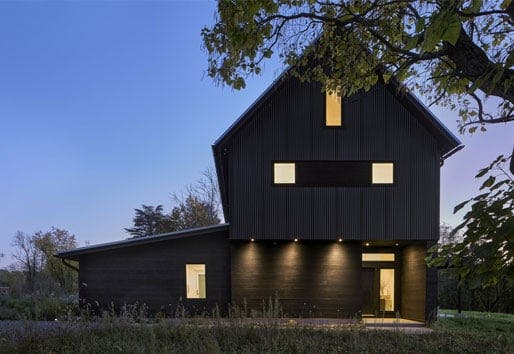 A black barn-style home silhouetted against an evening sky.