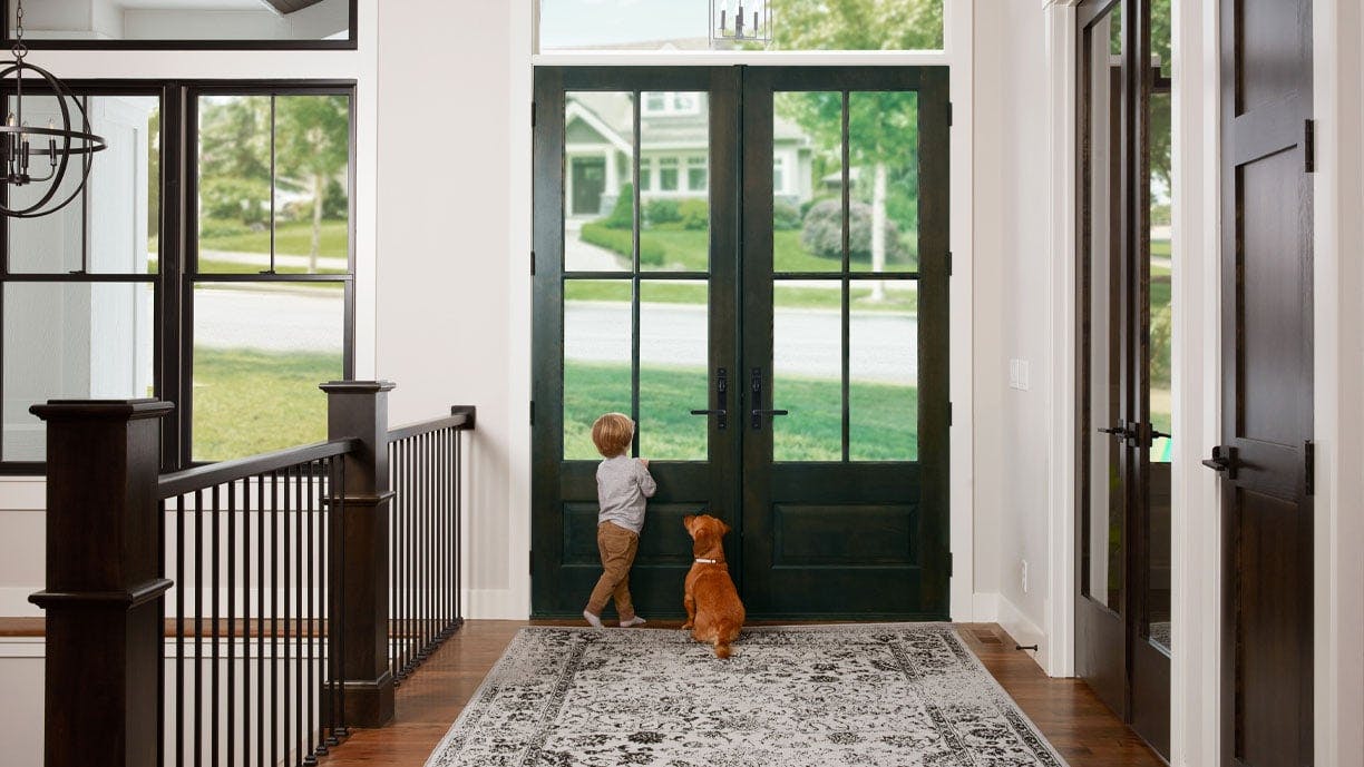 boy and dog standing at front entry door looking out